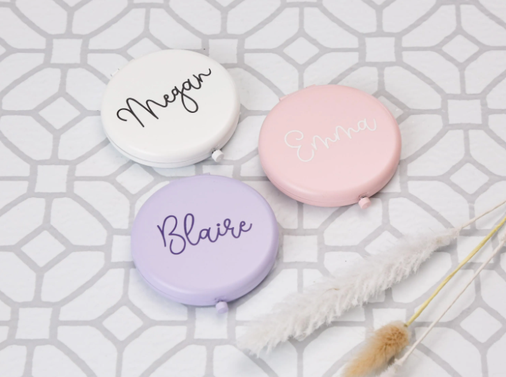 Three round compacts with names 'Megan', 'Emma', and 'Blaire' on a geometric patterned background.