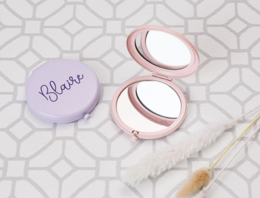 Compact mirror with purple case labeled 'Blair' on a geometric patterned background.