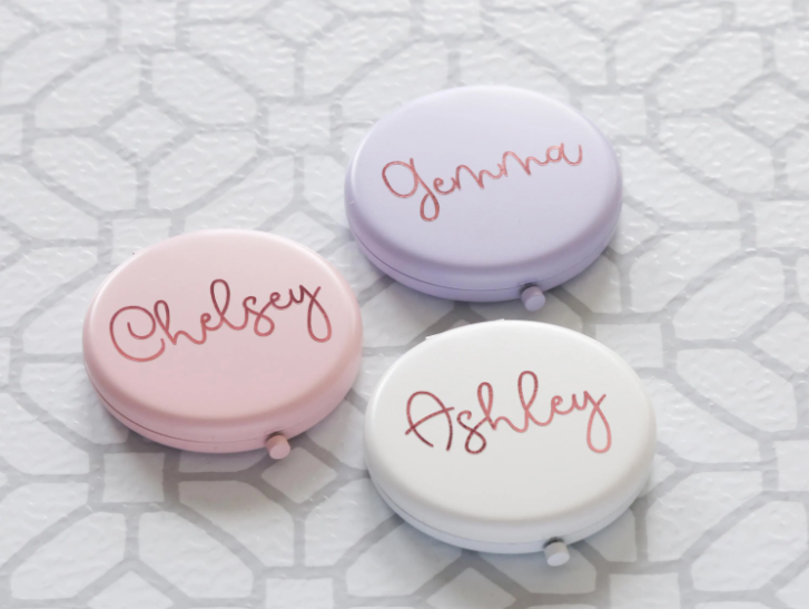 Three small round compacts with names 'Chelsey', 'Jenna', and 'Ashley' on a textured white background.