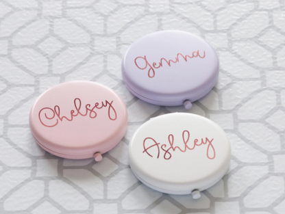 Three small round compacts with names 'Chelsey', 'Jenna', and 'Ashley' on a textured white background.